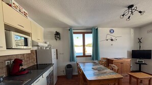 A compact kitchen with a microwave, stove, and sink. A dining table with chairs is in the center, and a television is on a stand to the right. - Beautiful 4 rooms in Superdévoluy - 8 pers., pets allowed (Le Dévoluy)