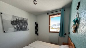 A bedroom with a bed, a window with curtains, a wall-mounted shelf, and a painting. - Beautiful 4 rooms in Superdévoluy - 8 pers., pets allowed (Le Dévoluy)