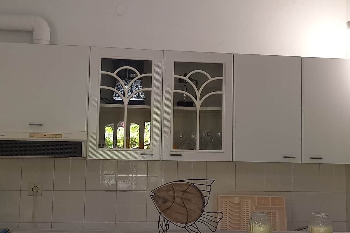 A kitchen with white cabinets, a window with decorative glass, and a white chair.