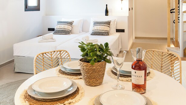 A neatly arranged dining area with a round table set for four, a potted plant, and a bottle of wine. - Sofia Studios (Skiathos)