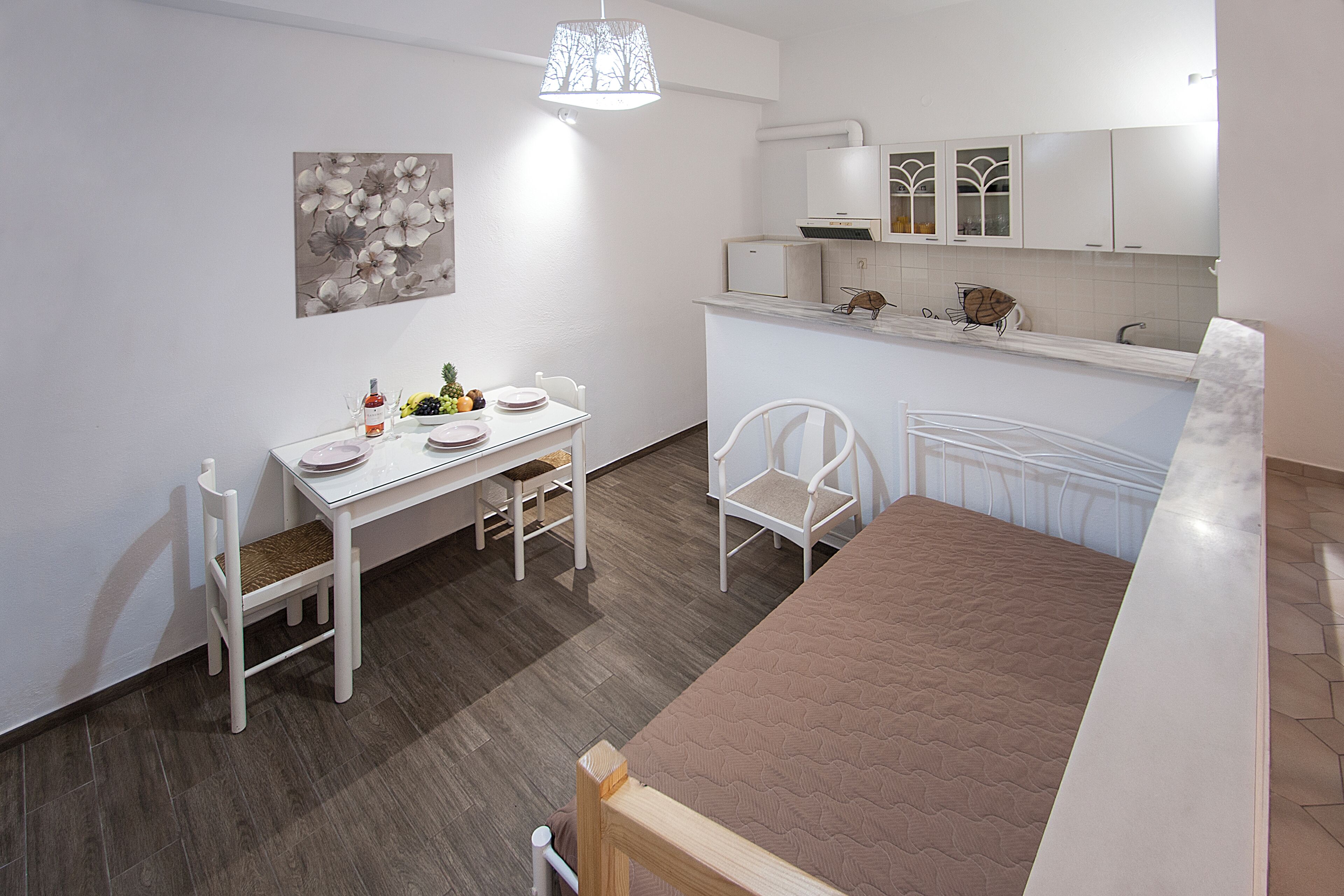 A compact room with a bed, a dining table with chairs, a kitchenette, and a wall-mounted artwork.