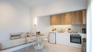 A modern kitchen with white cabinetry, a built-in oven, and a dining area with a white table and chairs. - Sofia Studios (Skiathos)