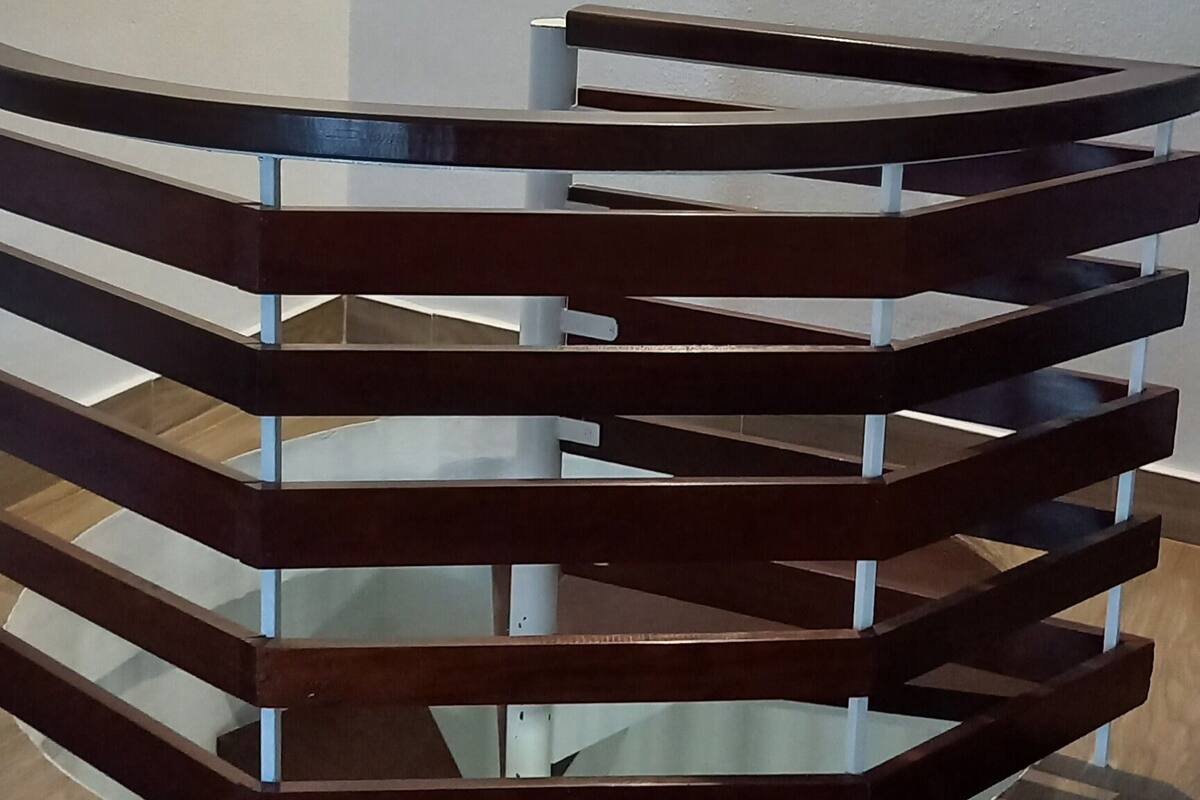 A modern staircase with a wooden handrail and glass steps, leading to a landing with a green emergency exit sign.