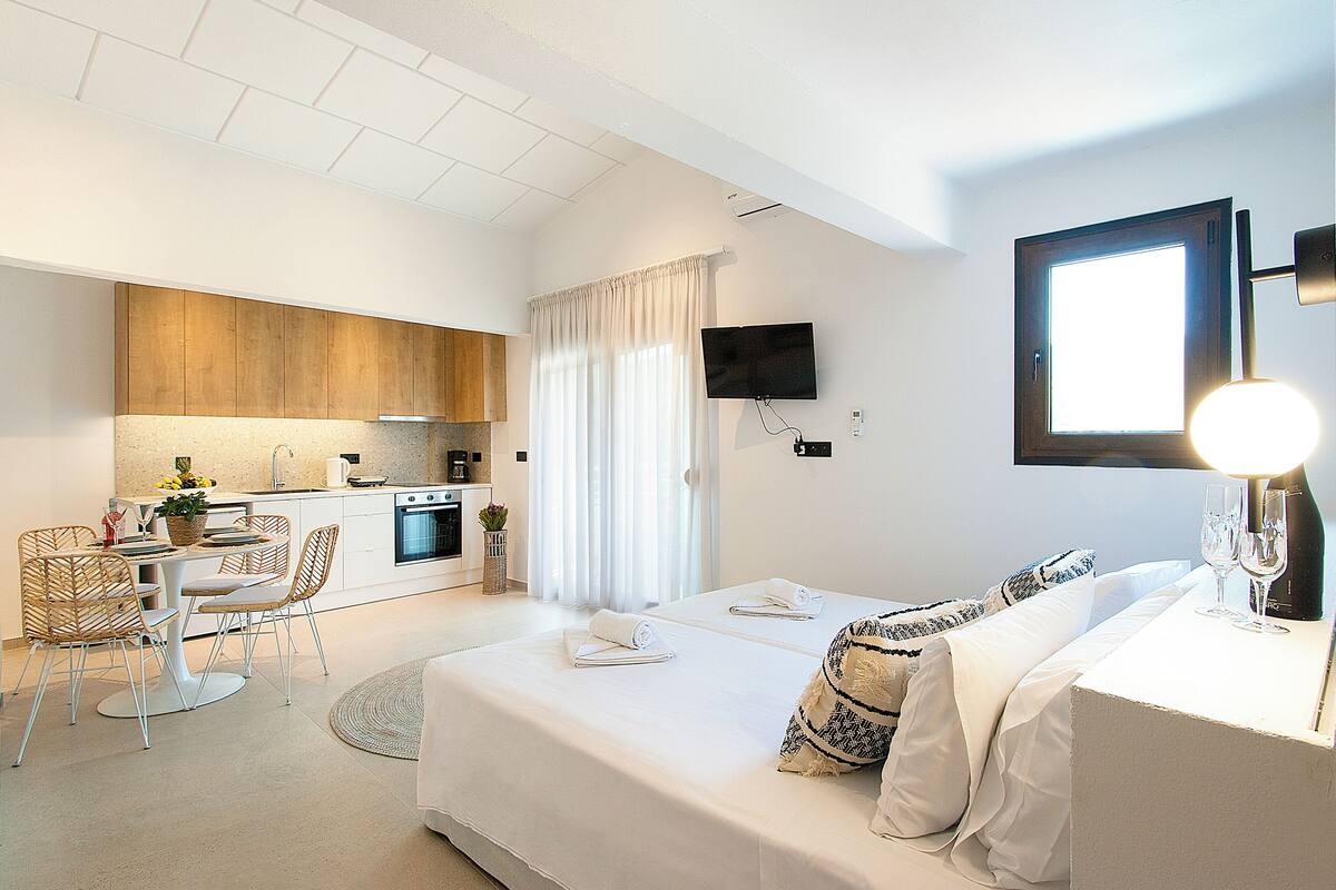 A modern hotel room with a bed, a desk, and a kitchenette.
