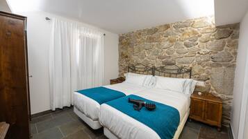 A bedroom with a stone wall, a bed with white bedding and a blue blanket, a hairdryer, and a wooden nightstand.