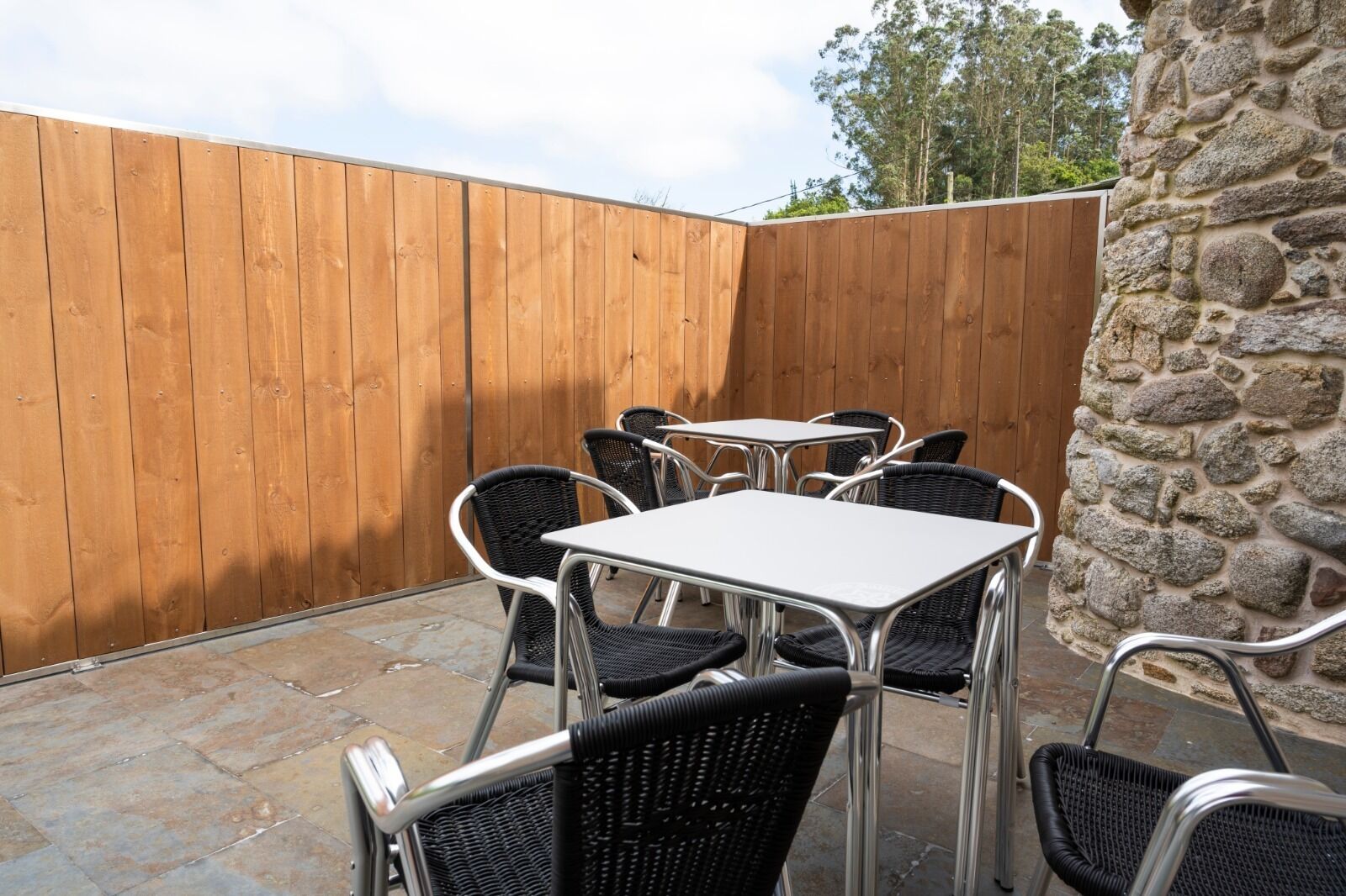 Eine Terrassenausstattung mit sechs Metalltischen und -stühlen, umgeben von einem Holzzaun und einer Steinmauer.