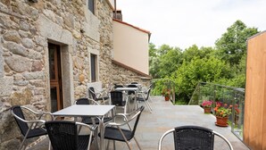 Eine Terrasse im Freien mit Steinmauern, Metalltischen und -stühlen sowie Blumentöpfen.