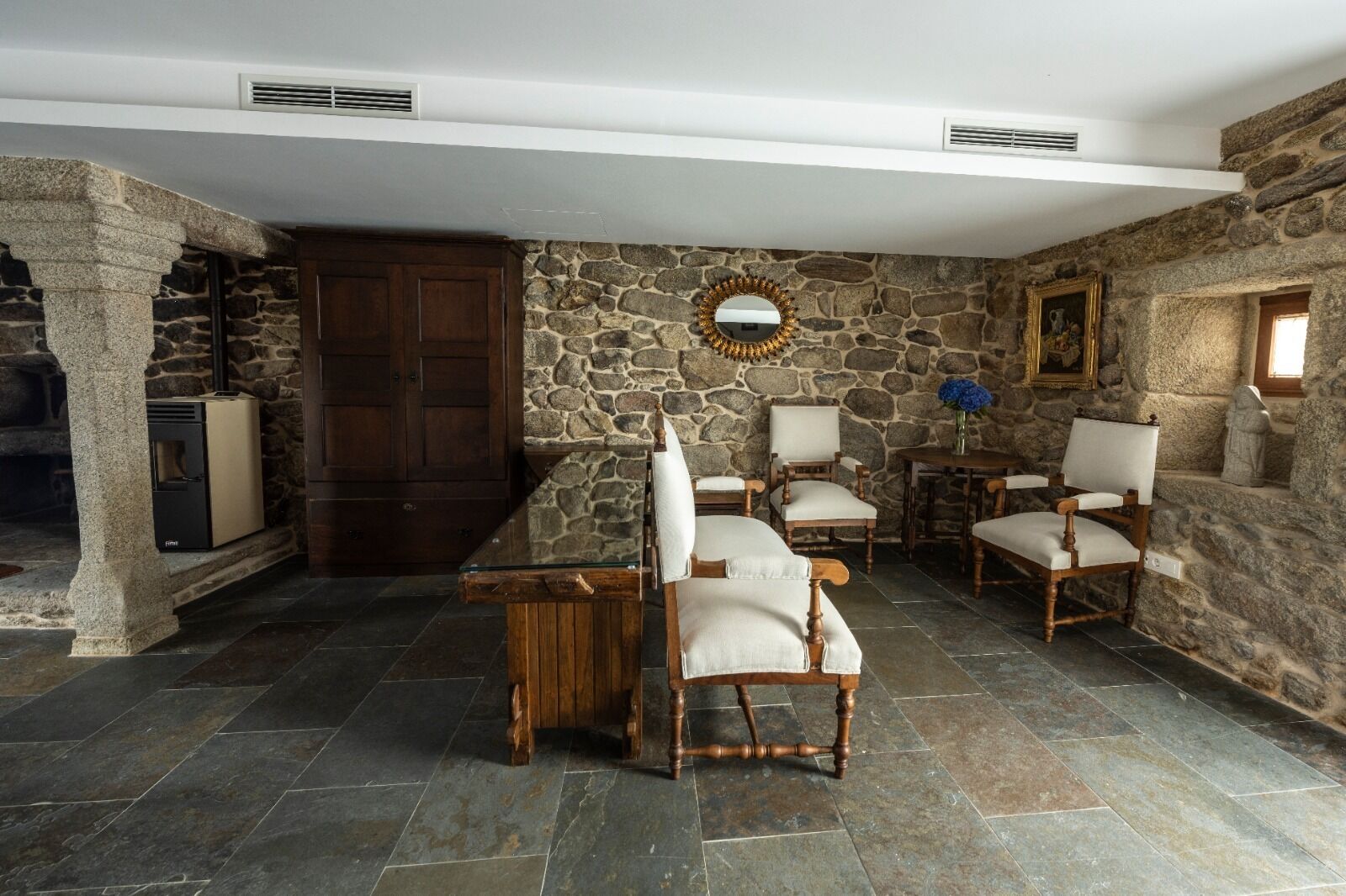 A stone-walled room with a stone fireplace, a wooden table, and four upholstered chairs.