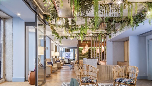 Un vestíbulo moderno con mobiliario de mimbre, una recepción y plantas colgantes.