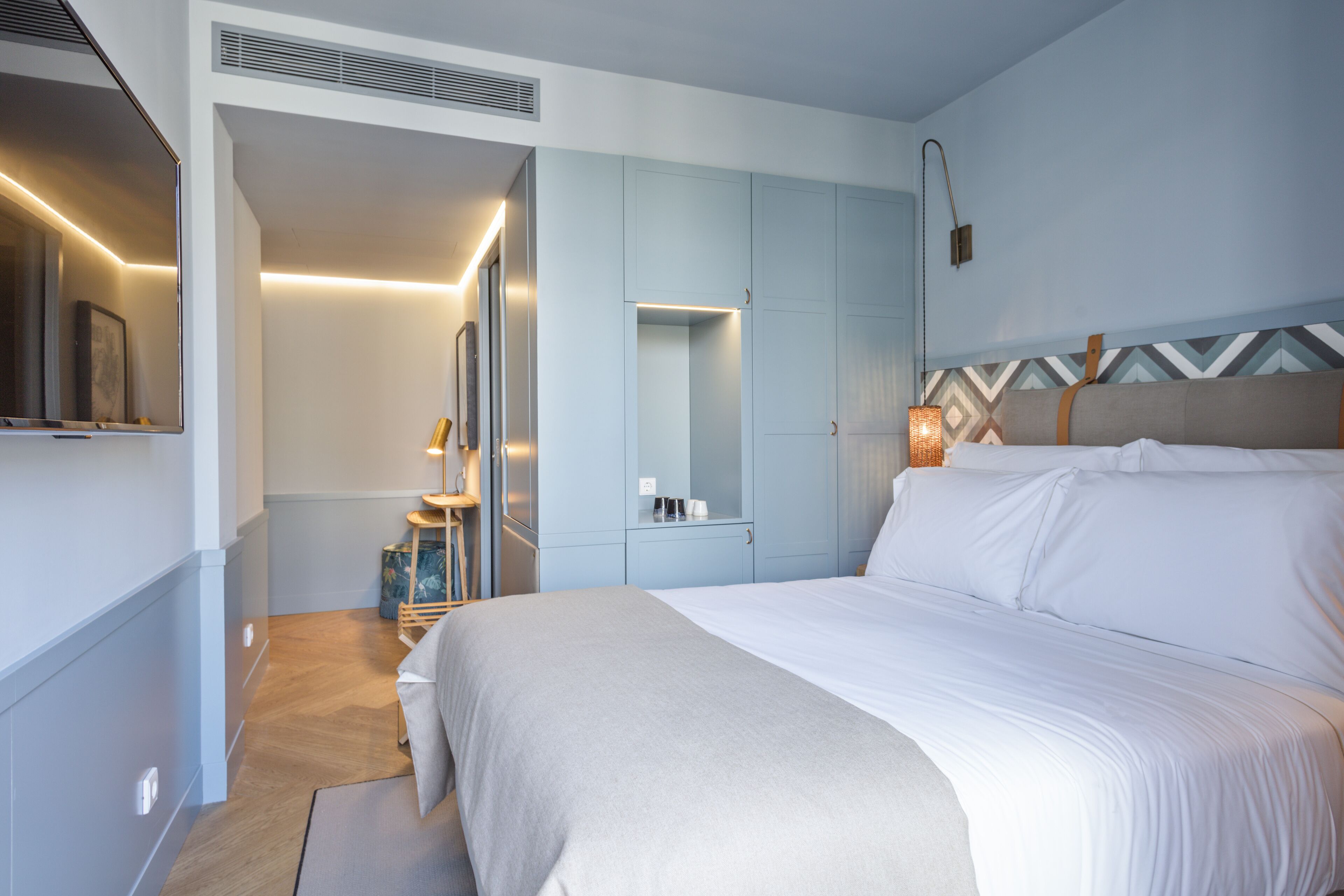 A modern hotel room with a bed, a wardrobe, a mirror, and a bedside table.