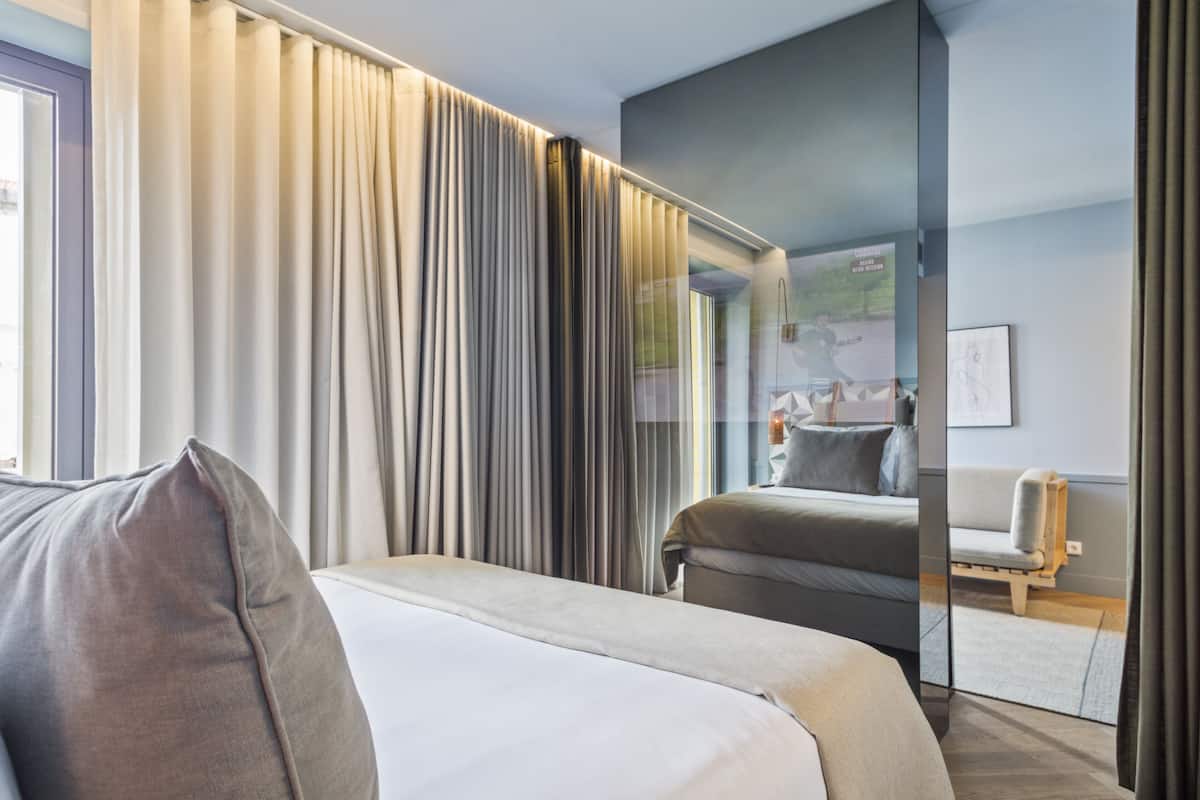 Een moderne hotelkamer met een groot bed, een bank en een spiegel die de kamer weerspiegelt.