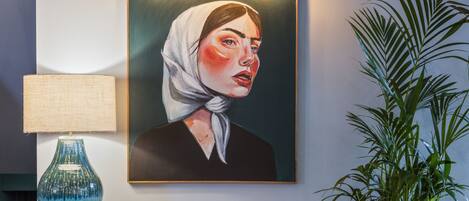 A painting on a wall, a lamp on a cabinet, and a plant beside the cabinet.