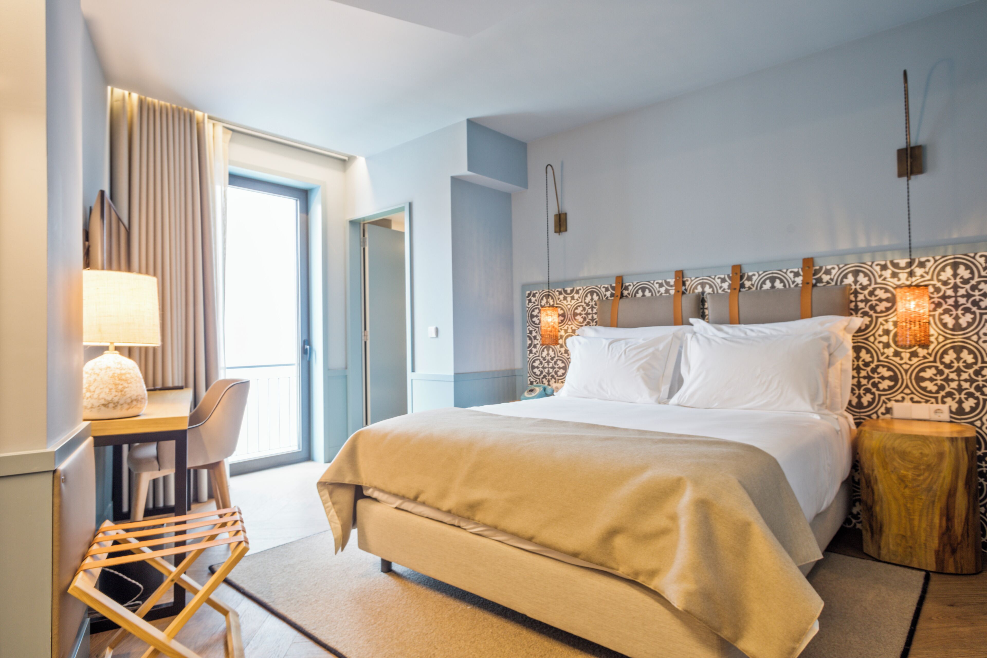 Une chambre d’hôtel moderne avec un grand lit, un bureau avec une lampe et une vue sur l’extérieur.