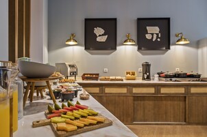 Un buffet della colazione con diversi cibi, un angolo caffè e opere d'arte appese al muro.