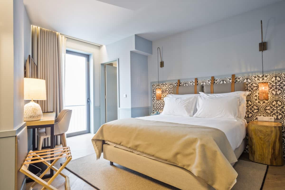 Een moderne hotelkamer met een groot bed, een bureau met lamp en uitzicht op de omgeving.