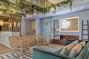 A lobby with wicker chairs, a checkered floor, a green sofa, and a wall with a 'STAY HERE PORTO LIVES' sign.