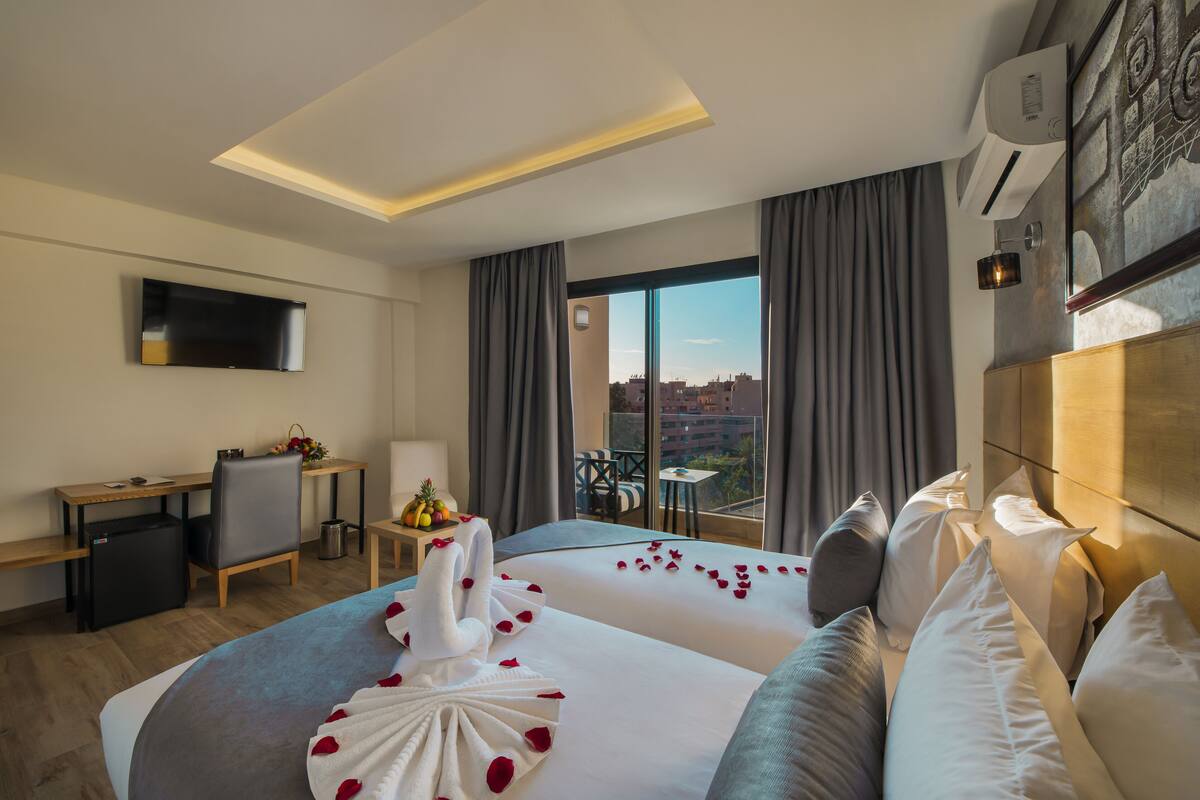 Ein Hotelzimmer mit Bett, Schreibtisch, Fernseher und einem Balkon mit Blick auf die Stadt.