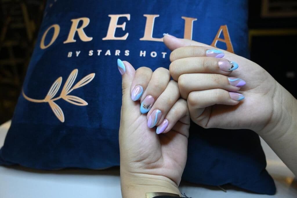 Two hands with painted nails resting on a pillow with the text 'ORELLIA BY STARS HOT'.