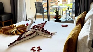 A hotel room with a bed, a chair, a table with a fruit bowl and a bottle, and a balcony with a view of buildings. - Stars Hotel (Marrakech)
