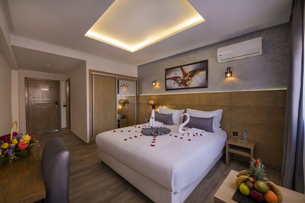 Habitación de hotel con una cama grande, una mesita de noche con frutero, aire acondicionado de pared y luz de techo.
