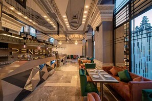 Un amplio vestíbulo de hotel con área de bar, distribuciones de asientos y vistas al exterior.