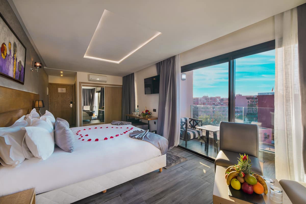 Ein modernes Hotelzimmer mit einem großen Bett, einem Essbereich und einem Balkon mit Blick auf die Stadt.