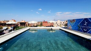 A clear swimming pool with lounge chairs and umbrellas, surrounded by buildings and a Stars Hotel sign. - Stars Hotel (Marrakech)