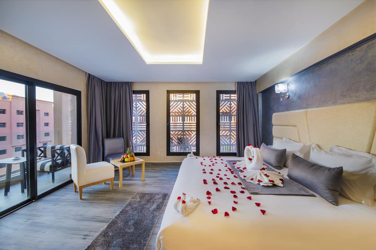 Ein Hotelzimmer mit einem großen Bett, einer Sitzecke mit Tisch und einem Balkon mit Blick auf Gebäude.