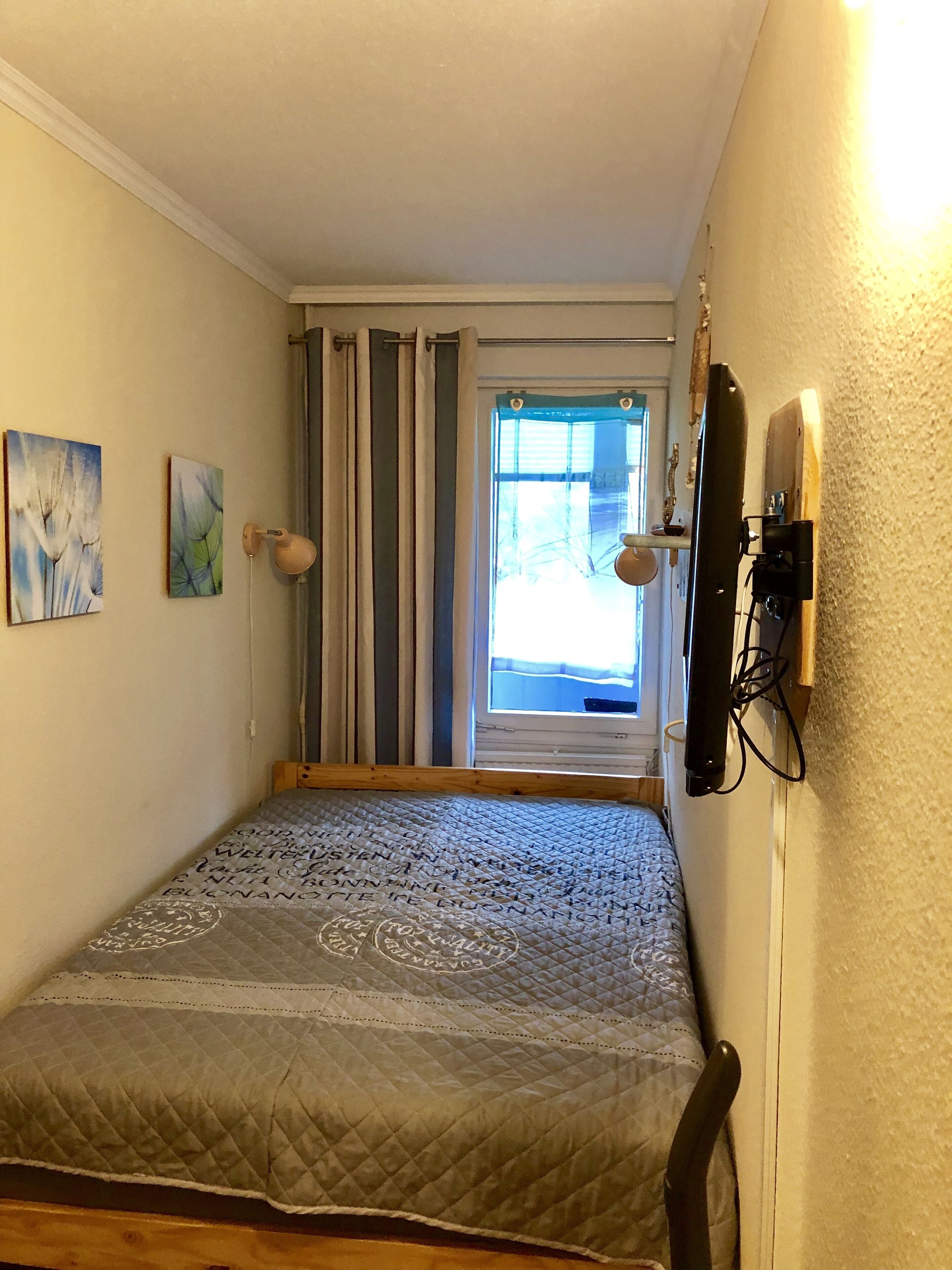 Een slaapkamer met een bed, een raam met gordijnen, een wandlamp en twee schilderijen.