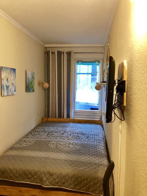 A small bedroom with a bed, a window with curtains, a wall-mounted lamp, and two paintings. - Apartment with loggia in a quiet complex, about 10 minutes walk to the (Holm)