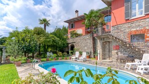 A pool area with a stone wall, a red building, and a clear sky.