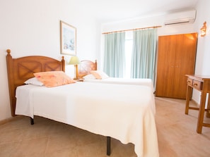 A bedroom with two beds, a wooden wardrobe, a bedside table, and a wall-mounted air conditioner. - Apartamentos Quinta da Praia (Portimão)