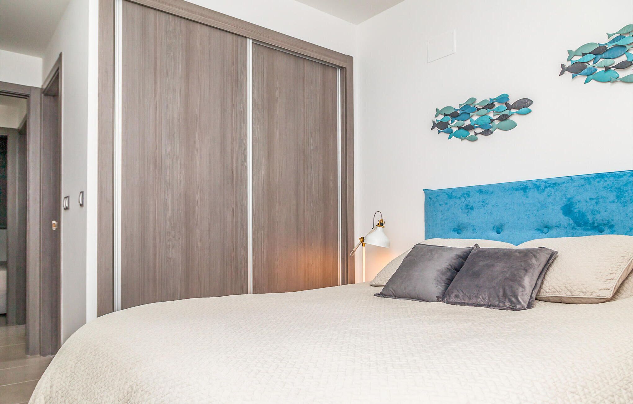 A bedroom with a large bed, a wooden wardrobe, a wall-mounted lamp, and decorative fish wall art.
