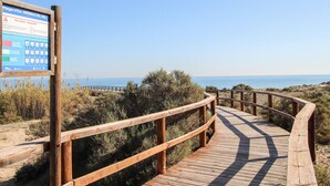 A wooden boardwalk leading to a beach with a signboard.