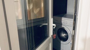 A laundry room with a washing machine and dryer, a door with a handle, and a window with a frosted glass panel. - 2-bed Apartment (Kingston Upon Thames)