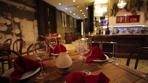 Een restaurantscène met gedekte tafels, wijnkannen en een bar op de achtergrond.