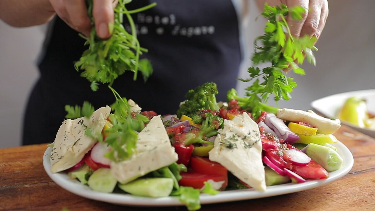 A person garnishing a salad with fresh herbs.