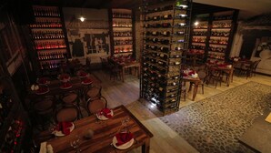 Een restaurant met meerdere eettafels, stoelen en een wijnrek vol flessen.