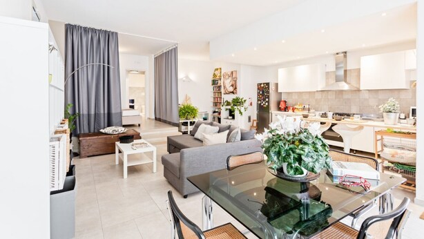 A modern living room with a glass dining table, grey sofa, and a kitchen area with white cabinets and appliances. - GuestHost - Large and bright 90sqm open space, with independent entrance, garden and private parking, located on the ground floor of a villa in the north area of Catania, just 15 minutes by car from the historic center.The apartment is equipped with all  (Catania)