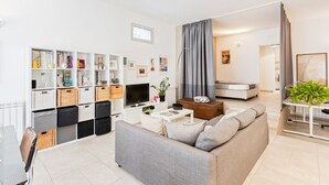 A modern living room with a sofa, coffee table, TV, and a bookshelf. - GuestHost - Large and bright 90sqm open space, with independent entrance, garden and private parking, located on the ground floor of a villa in the north area of Catania, just 15 minutes by car from the historic center.The apartment is equipped with all  (Catania)