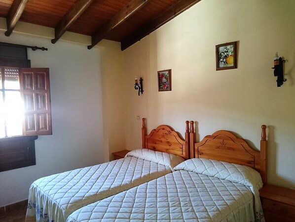 A bedroom with two wooden beds, a window with wooden shutters, and a wall-mounted light fixture.