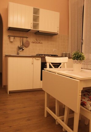 A compact kitchen with white cabinetry, a stove, and a dining area with a chair and table.