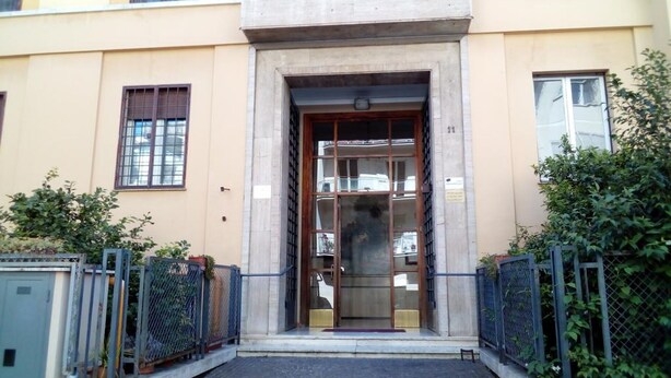 Une entrée d’immeuble avec un arc en béton, des portails en métal et un chemin pavé menant à la porte.