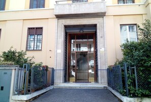 A building entrance with a concrete archway, metal gates, and a paved pathway leading to the door.