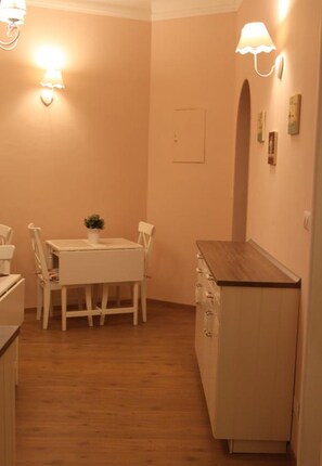 A small, cozy room with a wooden floor, a white table with chairs, a small cabinet, and wall-mounted lamps.