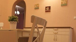 Un coin repas avec une table en bois, une chaise dotée d’un coussin à motifs floraux, un meuble avec des tiroirs et un luminaire fixé au mur.