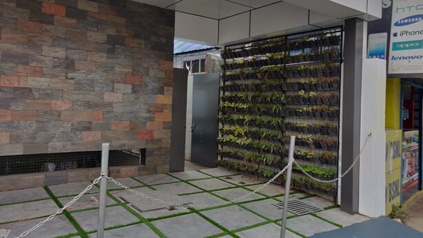 A modern building exterior with a stone wall, a vertical garden, and a chain barrier. - Thulasi Inn (Kanayannur)