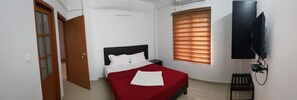 Une chambre à coucher avec un lit, une télévision, une fenêtre avec des stores et une porte.