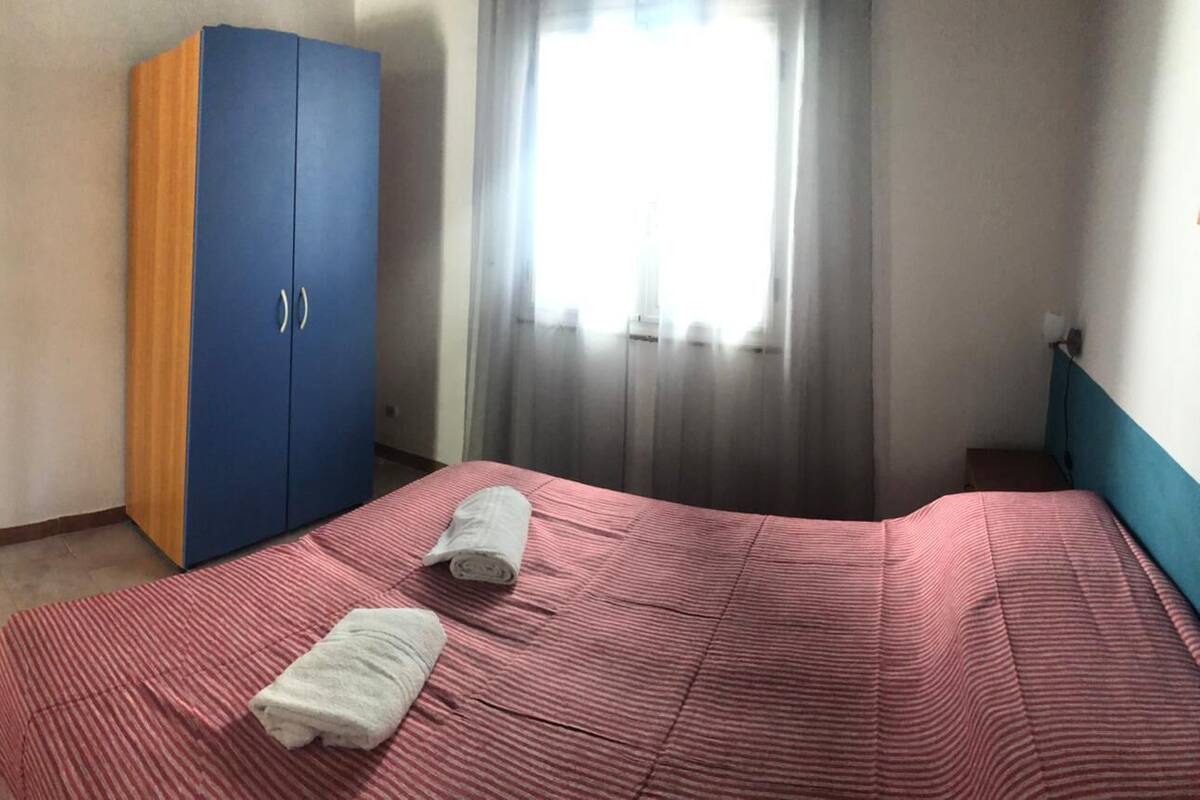 Une chambre à coucher avec un lit, deux serviettes, une armoire et une fenêtre avec des rideaux.