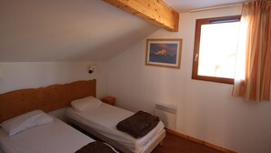Un dormitorio con dos camas individuales, una viga de madera en el techo, un radiador, una ventana con cortinas e imagen enmarcada en la pared.